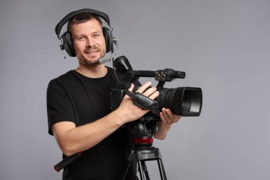 Profesyonel kameralı ve kulaklıklı bir adam gri arka planda.