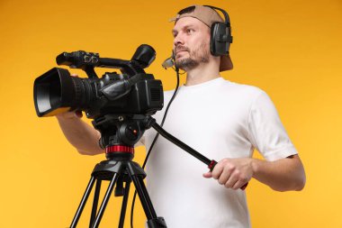 Profesyonel kamera ve turuncu arka planda kulaklığı olan bir adam.