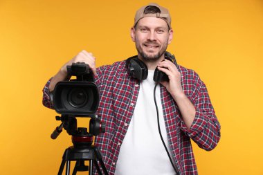 Profesyonel kamera ve turuncu arka planda kulaklığı olan bir adam.