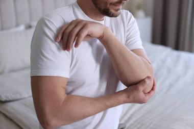 Evdeki yatakta dirsek ağrısı çeken bir adam, yakın plan.