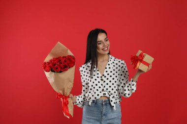 Kırmızı arka planda lale buketi ve hediye kutusu olan mutlu bir kadın. 8 Mart kutlamaları