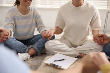 Grup psikoterapi seansı sırasında el ele tutuşan insanlar kapalı mekanda, yakın çekim