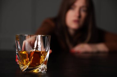 Alkol bağımlılığı. Ahşap masada bir bardak viskisi olan kadın, seçici bir odak noktası.