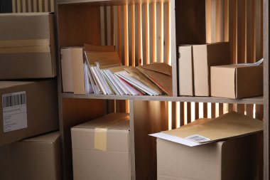 Postanedeki ahşap raflarda farklı kağıt zarflar ve paketler var.