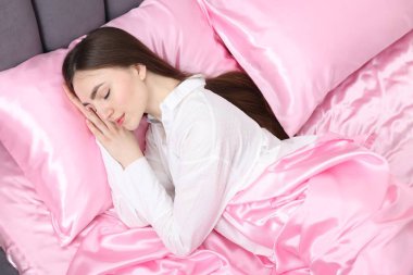 Yatakta pembe ipek çarşaflarla uyuyan bir kadın.