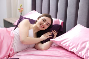 Yatakta pembe ipek çarşaflarla gülümseyen bir kadın.