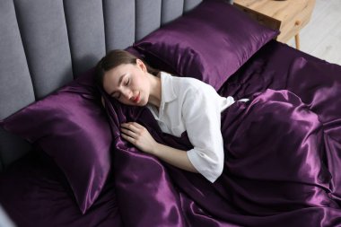 Mor ipek çarşaflarla yatakta uyuyan bir kadın.