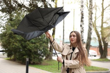 Şemsiyesi kırık bir kadın dışarıda rüzgarla savaşıyor.