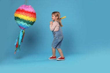 Mutlu kız parlak pinyatayı açık mavi arka planda kırıyor.