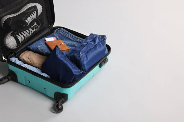 Packing cubes with clothes, sneakers, passport and ticket in suitcase on light background, space for text