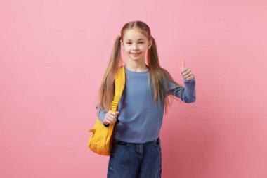 Sırt çantalı liseli kız pembe arka planda baş parmak gösteriyor.