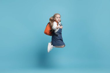 Sırt çantalı kız öğrenci açık mavi arka planda zıplıyor