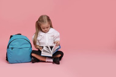 Sırt çantalı liseli kız pembe arka planda kitap okuyor. Metin için boşluk