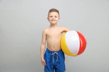 Teninde güneş kremi ve açık gri arka planda şişme top olan küçük bir çocuk.