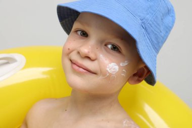 Teninde güneş kremi ve açık gri arka planda şişme yüzük olan küçük bir çocuk.