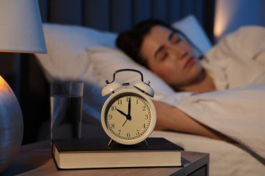 Evde uyuyan genç kadın, çalar saate ve kitaba odaklan.
