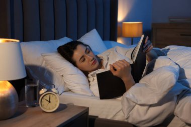 Evde yatakta kitap okuyan genç bir kadın.