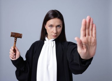 Elinde tokmak olan yargıç gri arkaplanda dur işareti yapıyor.