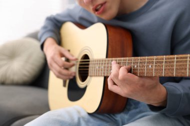 Genç adam kanepede gitar çalıyor, yakın plan.