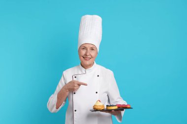 Profesyonel pasta şefi açık mavi arka plandaki tatlılara işaret ediyor.
