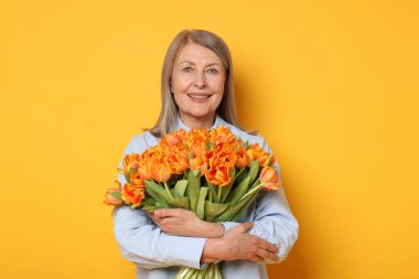 Sarı arka planda bir buket lale ile gülümseyen kadın.