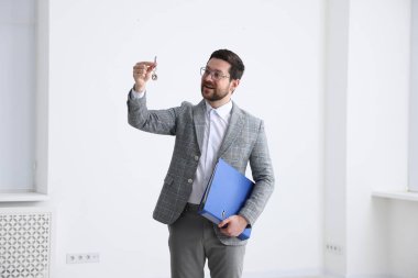 Emlakçının elinde ev şeklindeki anahtarlık ve klasör var.