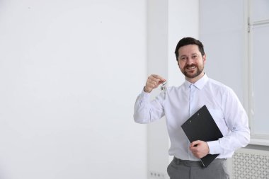 Emlakçının elinde anahtarlık, ev şeklindeki anahtarlık, kapalı alanda pano ve metin için yer var.