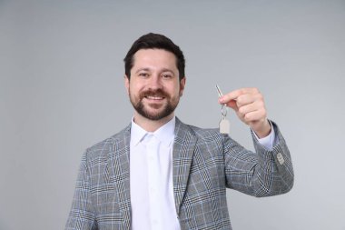 Emlakçının elinde anahtarlık açık gri arka planda ev şekilli anahtarlık var.