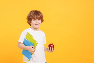 Turuncu arka planda kitapları ve elması olan şirin bir çocuk. Metin için boşluk