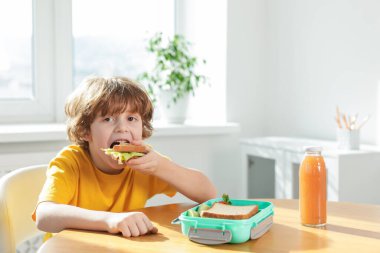 Okulun ahşap masasında yemek yiyen şirin küçük çocuk. Metin için boşluk
