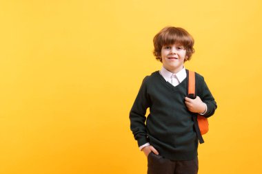 Turuncu arka planda sırt çantası olan tatlı bir okul çocuğu, mesaj için yer var.