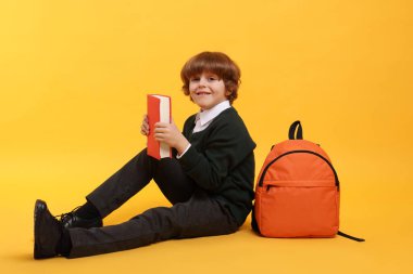 Sırt çantası ve turuncu arka plan kitabı olan tatlı bir okul çocuğu.