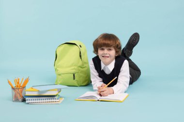 Sırt çantasında açık mavi arka planda çizim yapan sevimli bir okul çocuğu.