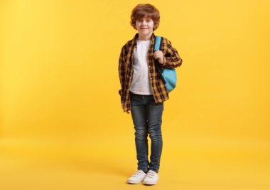 Sırt çantası ve turuncu arka plan kitabı olan tatlı bir okul çocuğu.