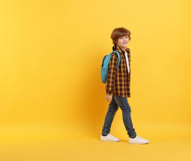 Turuncu arka planda sırt çantası olan tatlı bir okul çocuğu, mesaj için yer var.