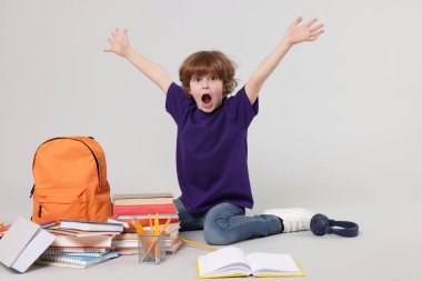 Sırt çantası, kitapları ve açık gri arka planda farklı kırtasiyeleri olan sevimli bir okul çocuğu.