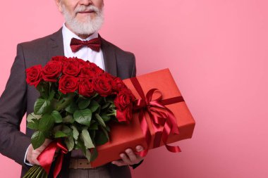 Kırmızı gül buketi ve pembe arka planda hediye kutusu olan son sınıf öğrencisi, yakın plan. Metin için boşluk
