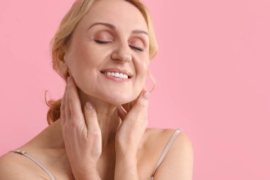 Pembe arka planda gülümseyen orta yaşlı kadın. Metin için boşluk