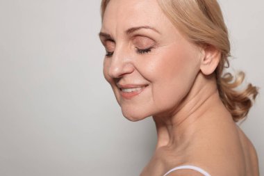 Gri arka planda gülümseyen orta yaşlı kadın. Metin için boşluk