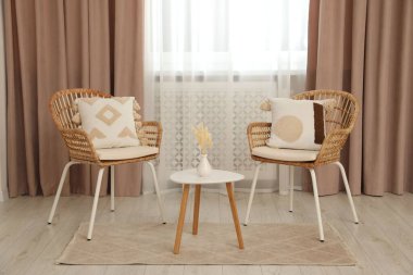 Pastel pencere perdeleri, ahşap masa ve rattan sandalyeli oturma odası.