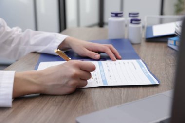 Klinikteki ahşap masada hastanın sağlık kartını dolduran doktor.