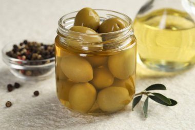 Kavanozda turşulu yeşil zeytin, beyaz desenli masada yağlı ve biberli mısır, yakın plan.