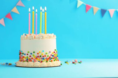 Renkli şekerli nefis bento keki ve açık mavi masada yanan mumlar. Metin için boşluk