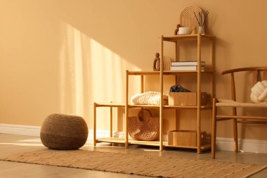 İçerideki bej duvarın yanında dekor, sandalye ve puf bulunan raf ünitesi.