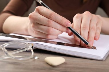 Ahşap masada cetvel ve kalemle çizim yapan kadın, yakın plan.