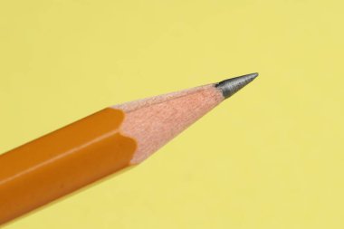 Sarı arka planda keskin bir grafit kalem, yakın plan.