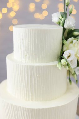 Gri arka planda çiçeklerle süslenmiş enfes düğün pastası. Bulanık ışıklar, yakın plan.