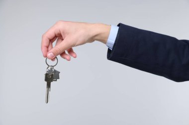 Emlakçı elinde ev şekilli anahtarlık açık gri arka planda, yakın plan.