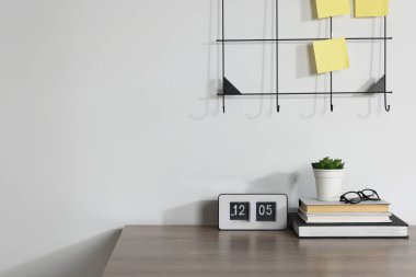 Kırtasiye, ters saat, çiçek dekoru ve beyaz duvarın yanındaki ahşap ofis masasında gözlük.