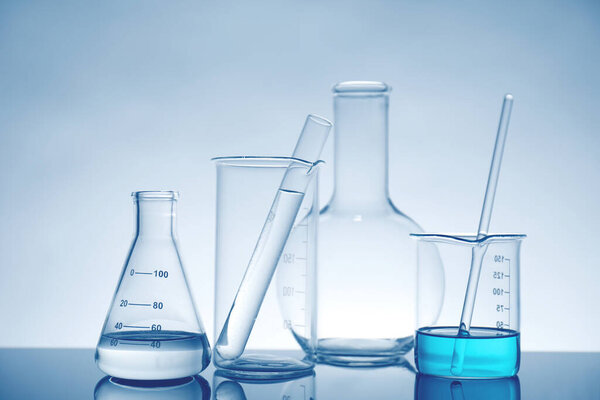 Laboratory glassware with liquid on mirror surface against light background